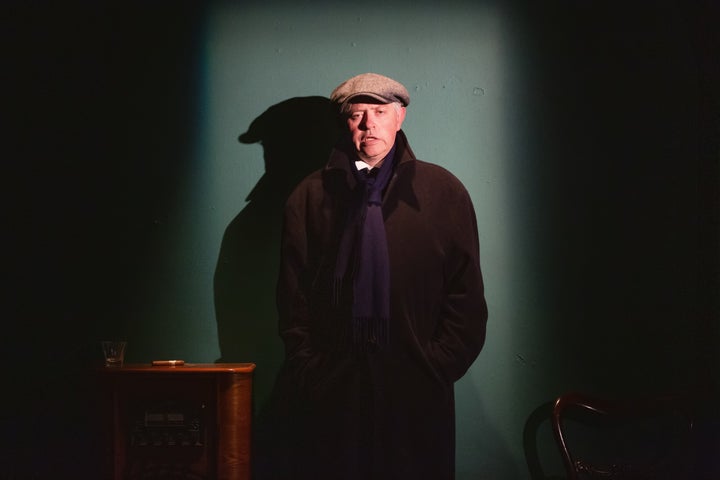 A man in dark overcoat and cap is talking
