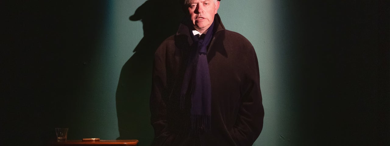 A man in dark overcoat and cap is talking