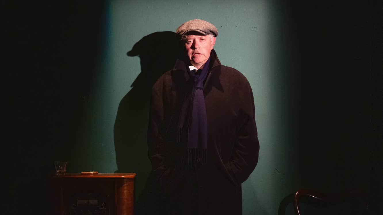 A man in dark overcoat and cap is talking