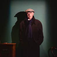 A man in dark overcoat and cap is talking