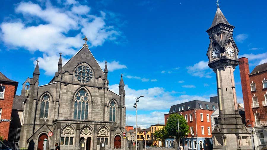 Tait's Clock in Limerick City with a church in the background against a blue sky