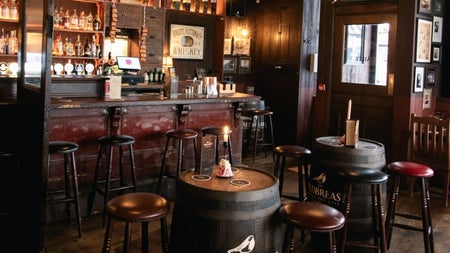 Traditional pub interior with a wooden bar high stools and barrel tables in a warmly lit setting