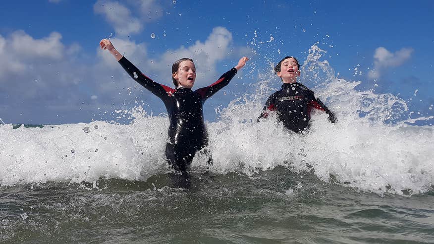 Two kids in wetsuits jumping through waves at Fermoyle Beach.