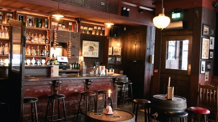 Interior of a traditional pub and bar with traditional dark wood tones and two wood barrels with stools as seating