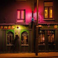 Exterior view of a bar illuminated at night with green frontage and traditional pub signage