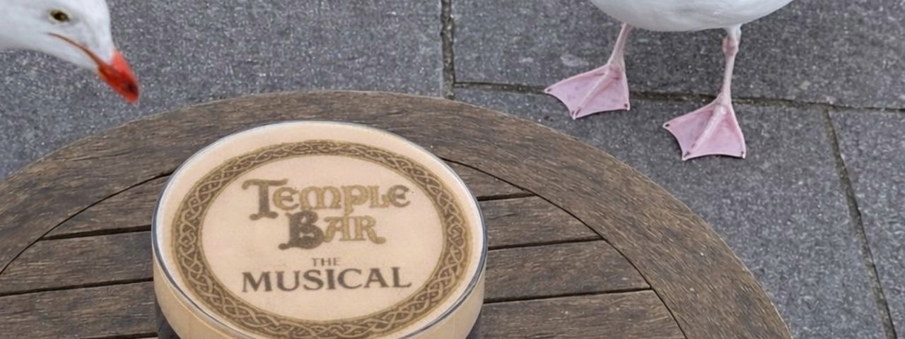 A pint of stout on round table outdoors being watched by 3 large seagulls.