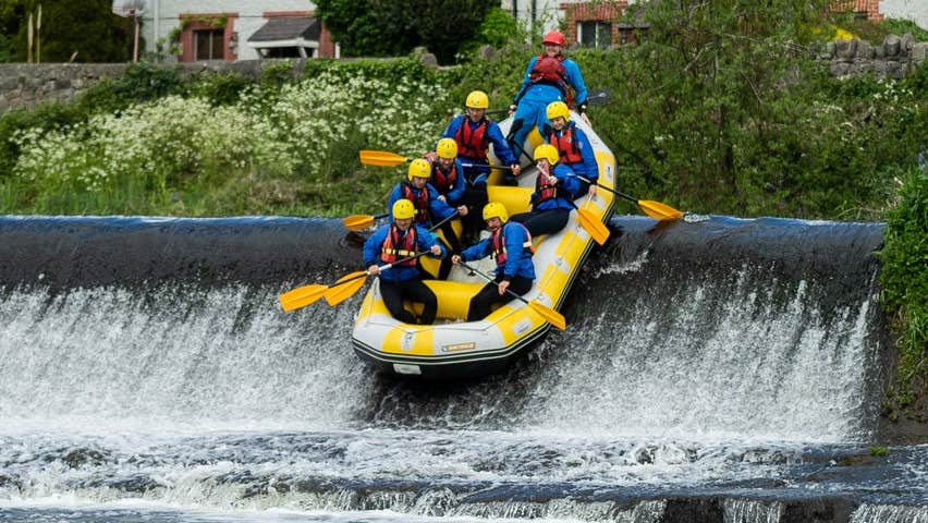 Eight people enjoying themselves rafting over a weir in a single raft