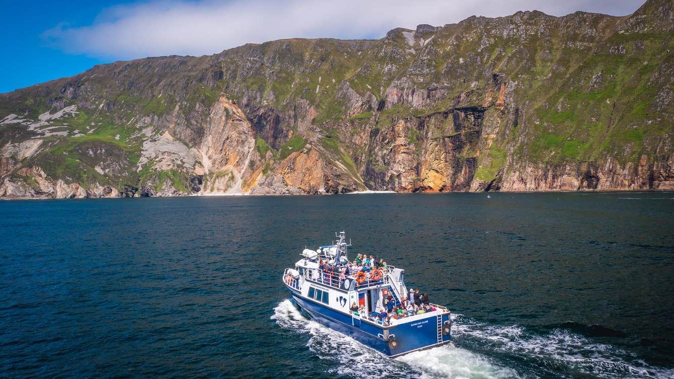 A boat with passengers heading towards high sea cliffs