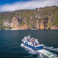 A boat with passengers heading towards high sea cliffs