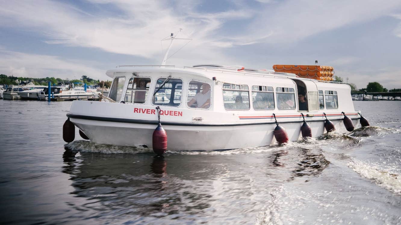 A white passenger boat named River Queen cruising on calm water