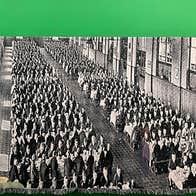 A black and white large textile hanging from rail with image of many rows of people in a large building, against bright green background.