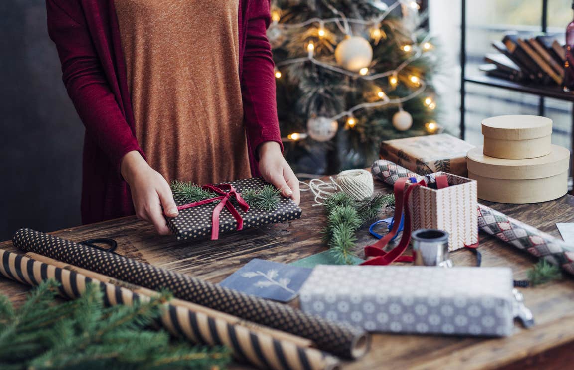 A person wrapping a present surrounded by wrapping paper and decorations