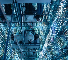 People in a glass lift surrounded by mirrors and lights