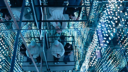 People in a glass lift surrounded by mirrors and lights