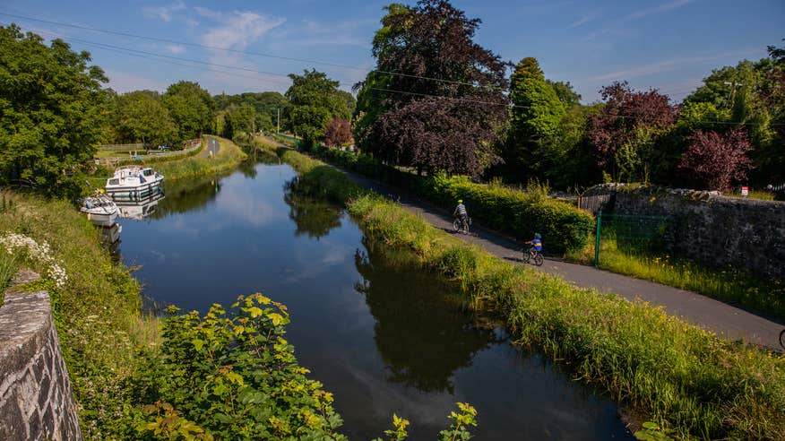 Two people cycling past canal boats on the Royal Canal Greenway in County Westmeath.