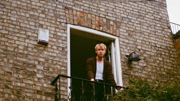 Looking up at a person standing on a small balcony on the end of a brick wall of a house