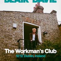 Looking up at a person standing on a small balcony on the end of a brick wall of a house