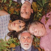 Looking down on 2 couples lying on ground covered in leaves with their heads all touching in a square shape