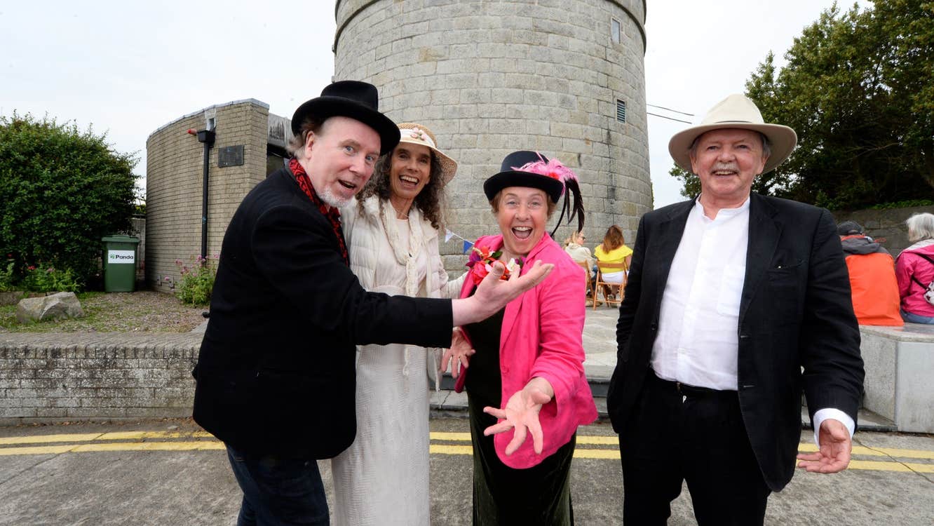 4 people in smart clothes standing in front of a round tower.