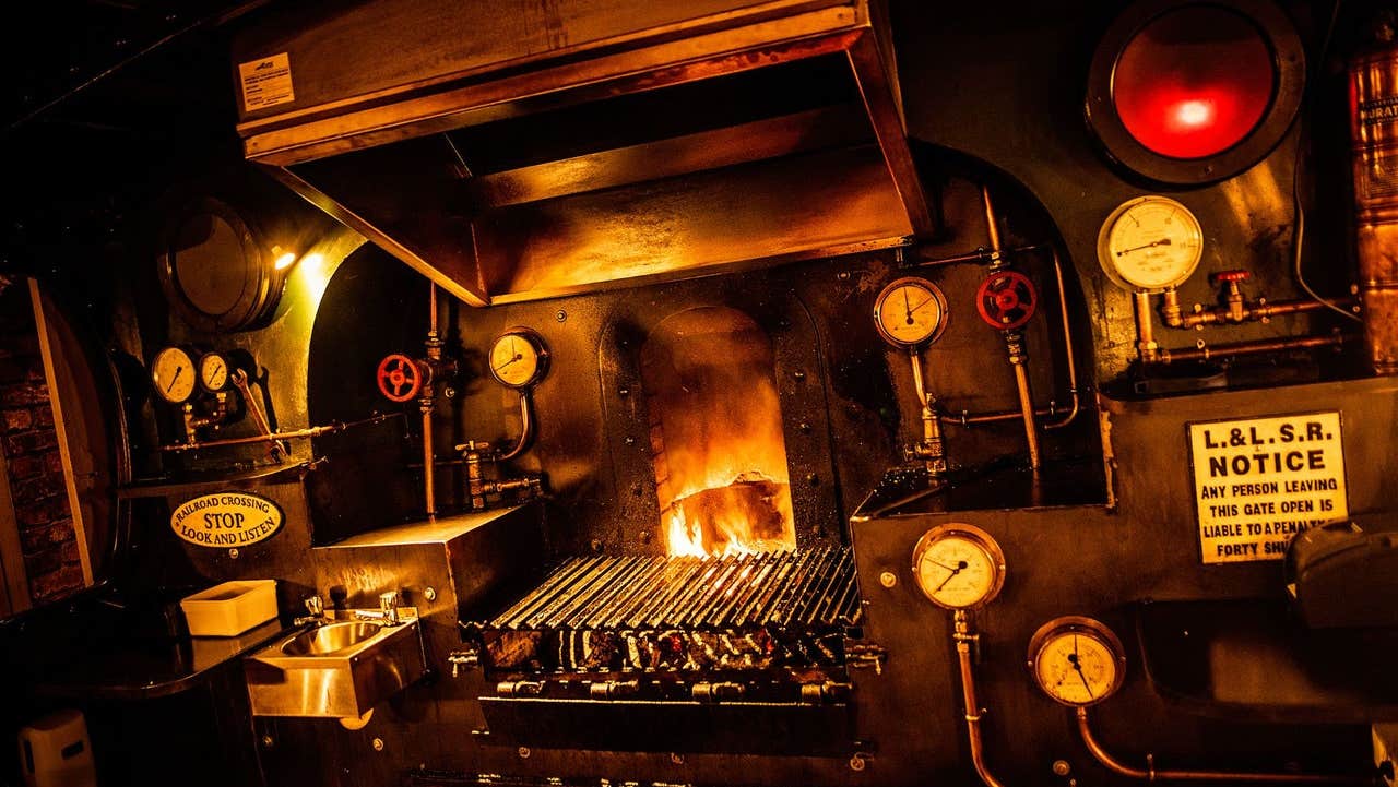 A firebox style grill glowing with open flames surrounded by vintage railway signage