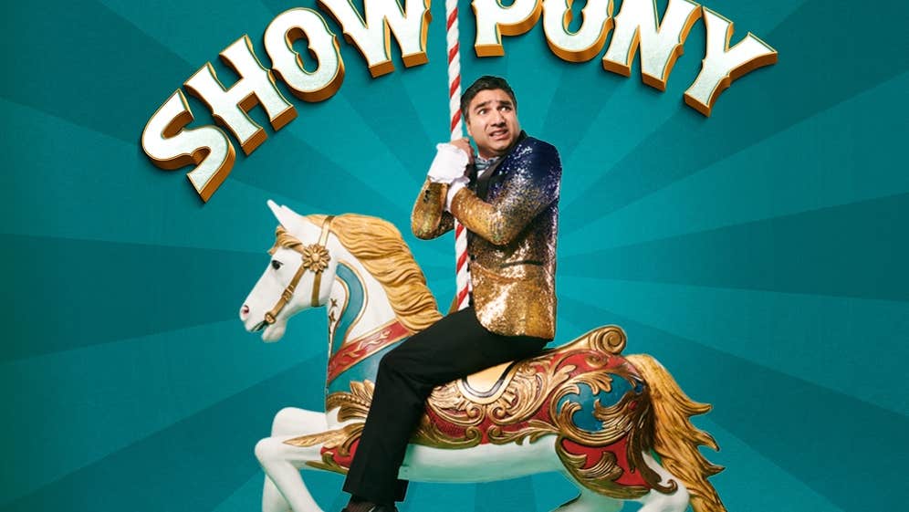 An anxious looking man in a gold sparkly jacket on the back of a decorated horse from a merry go round, clinging onto the stripy upright pole