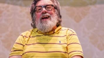 An Evening with Ricky Tomlinson, My Arse - a laughing older man with bushy beard seated with a mug on a table in front of him.