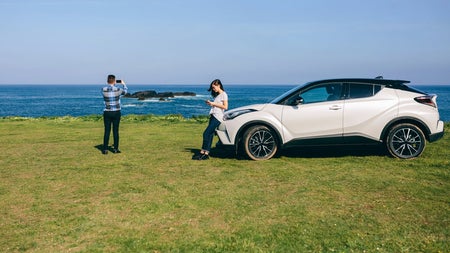 Two people at a scenic coastal location with their hire car