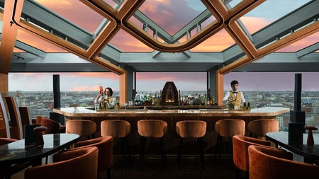 A rooftop bar interior and servers with panoramic views stretching across the city skyline at sunset