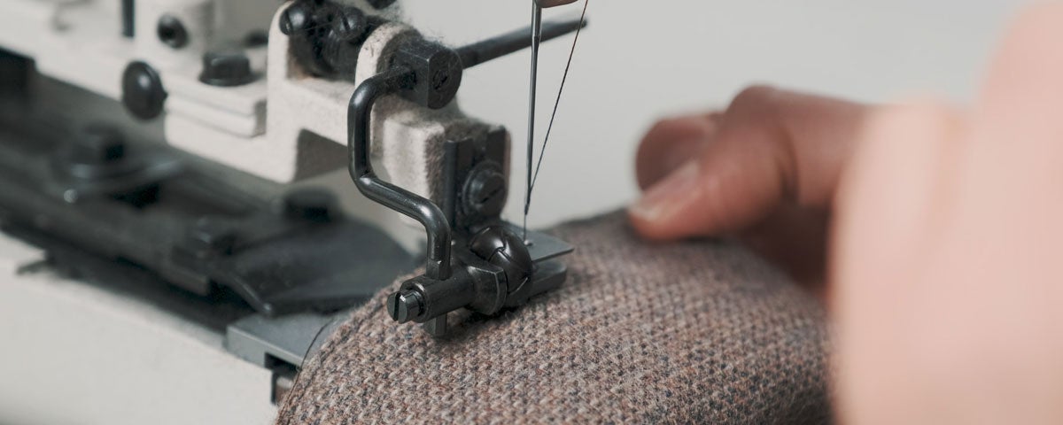 A close up of someone holding tweed cloth as a sewing machine stitches a seam