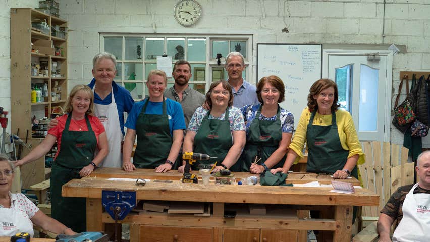 A group of people posing for a picture in aprons in front of a woodworking bench