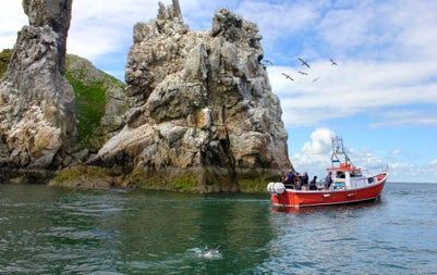 A boat with passengers passing by a rocky cliff
