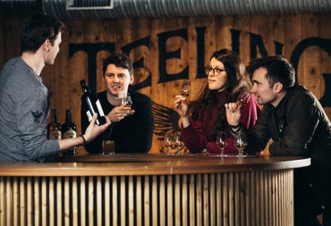 Four people standing at a wooden bar holding glasses and a bottle