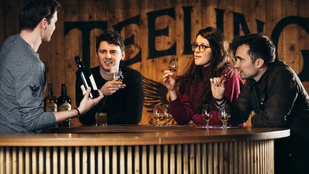 Four people standing at a wooden bar holding glasses and a bottle