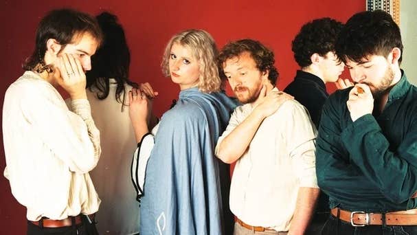 Group of 5 people standing, some facing in different directions with only 1 person looking directly at the camera.