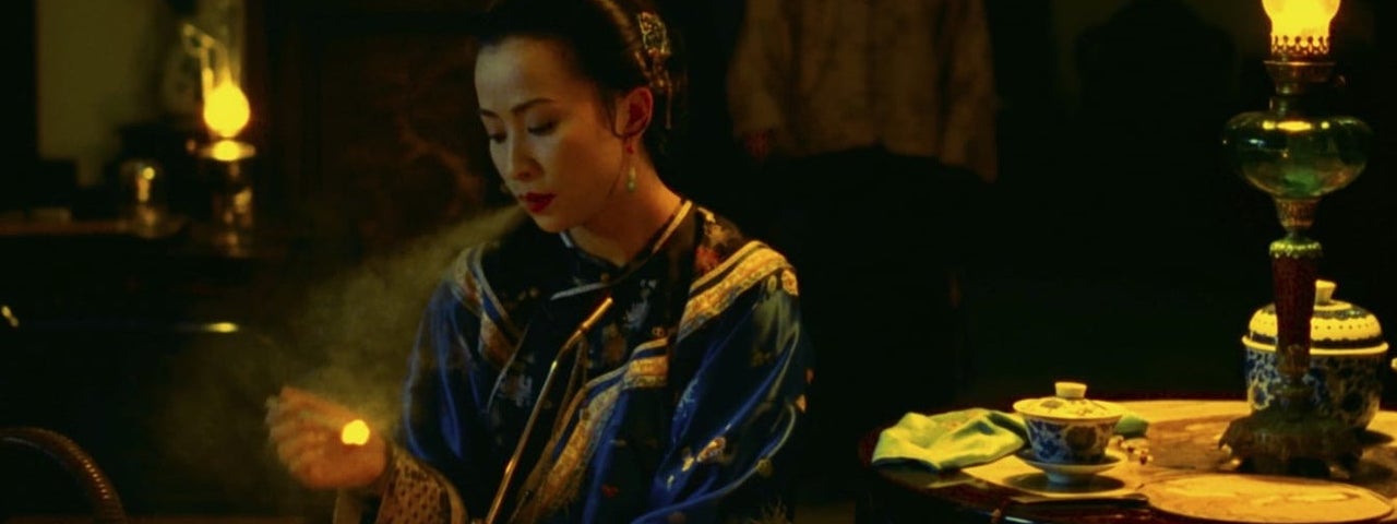 A Chinese woman is a well-made gown is sitting alone at a table. Her posture suggests sadness.