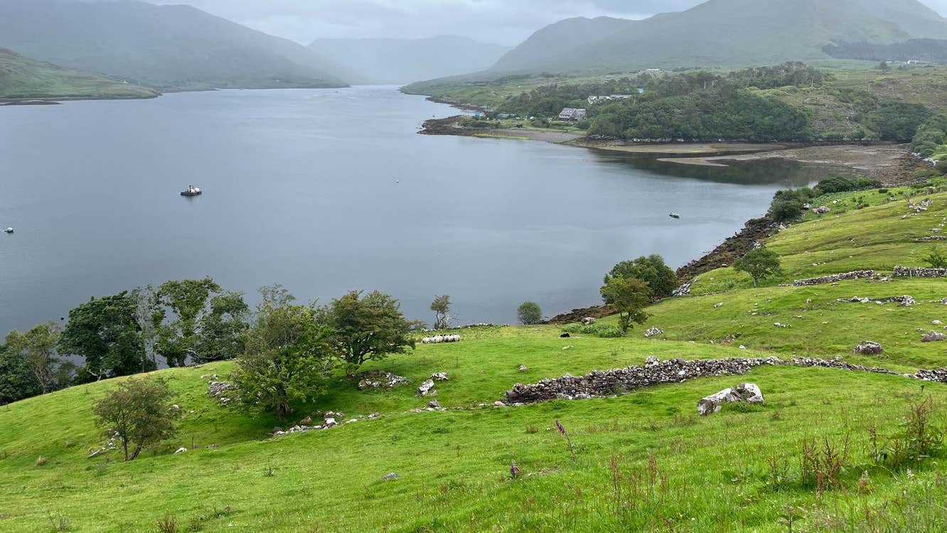 A lake by green fields with misty mountains in the background