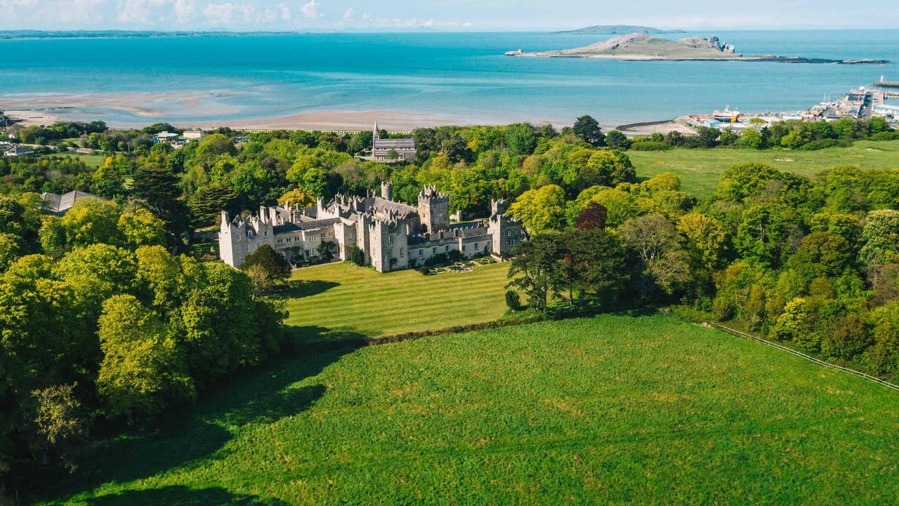 Aerial view of castle with green fields and coastal background