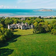 Aerial view of castle with green fields and coastal background