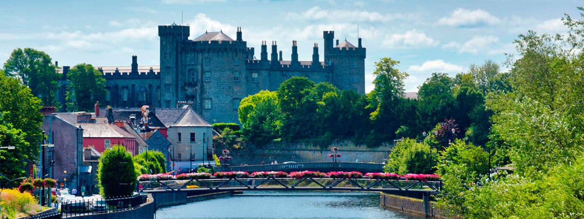 Kilkenny Castle with the River Nore and a pedestrian bridge with flowers