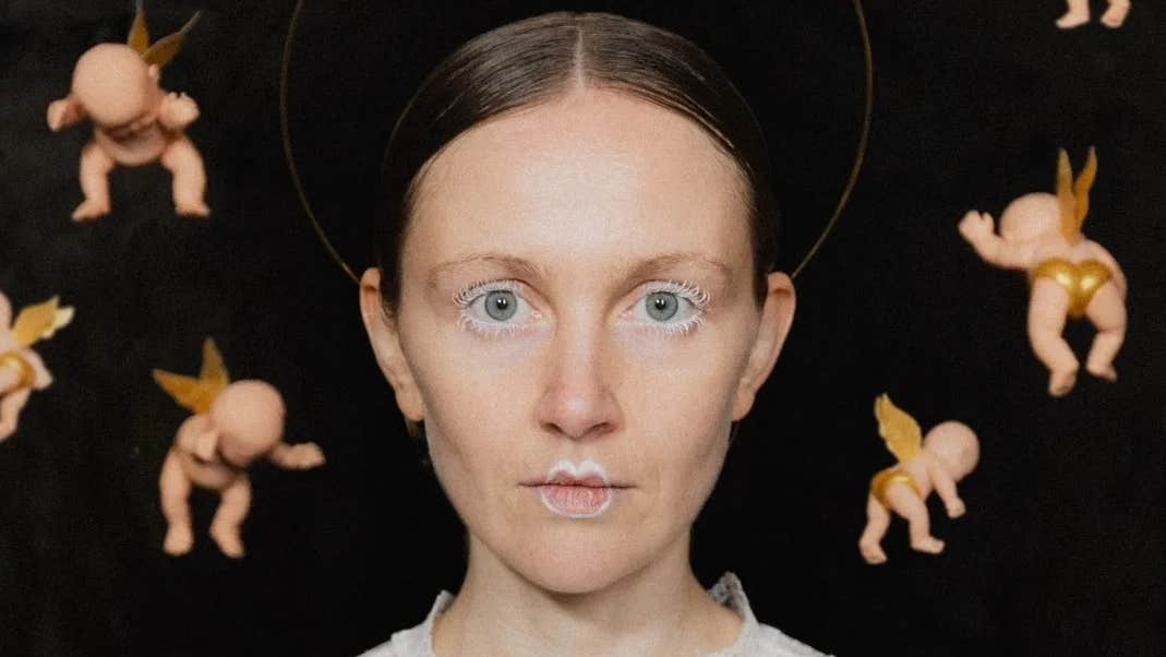 Electro folk musician Frankie Archer, a woman with hair pulled back from face looking directly ahead with white painted eyelashes and lips