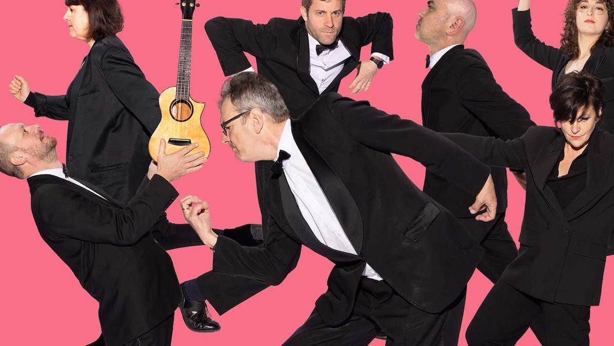 A group of people in black suits in various random poses against pink background.