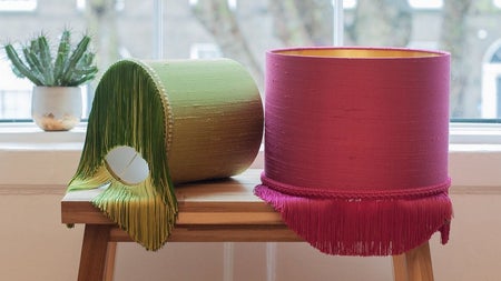 Two colourful fringed lampshades on a bench by a bright window