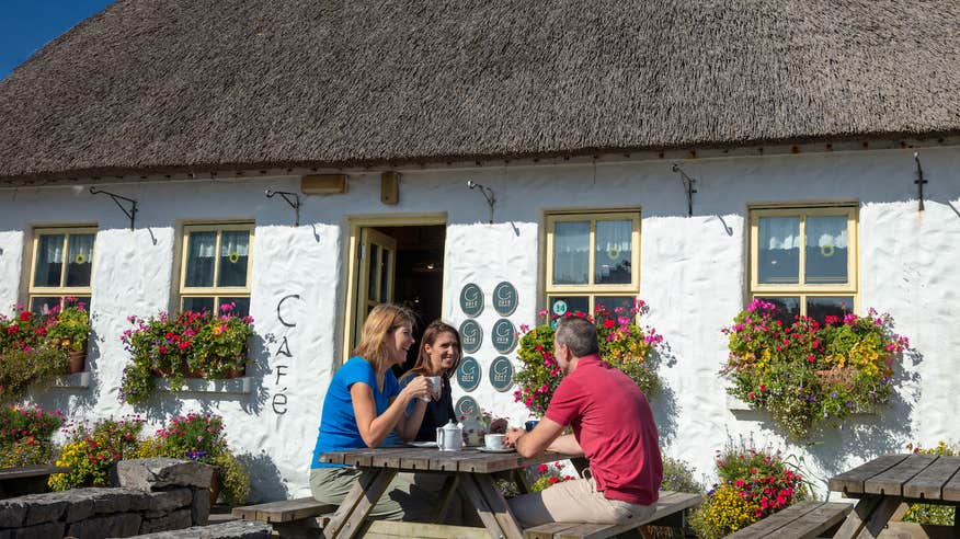 Three people sitting on a picnic table outside of Teach nan Phaidí in County Galway.