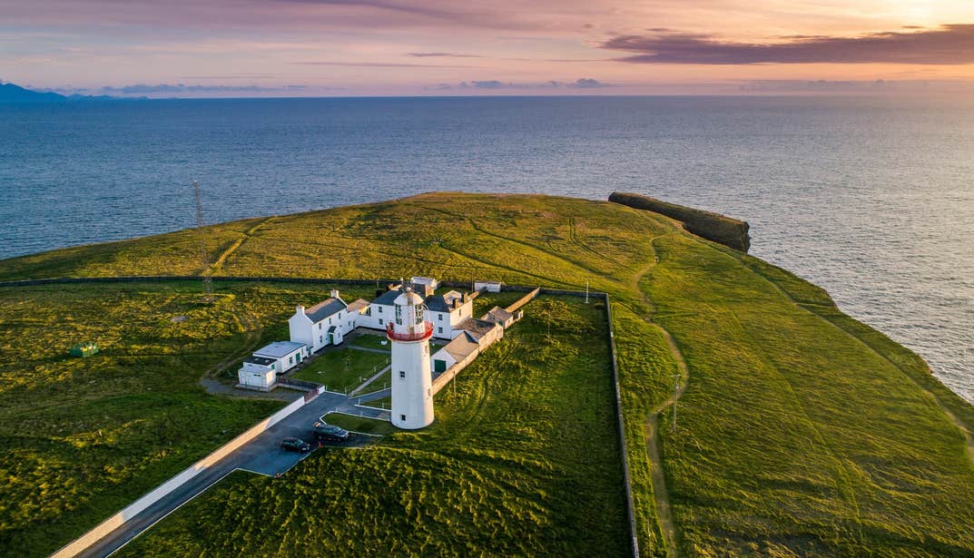 An aerial view of Loop Head Lighthouse from land at sunset