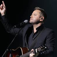 A man playing guitar with a mic on a stand and his right arm raised pointing up into the air.