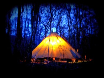Axe Club view of a tentipi with campers inside at night in a forest