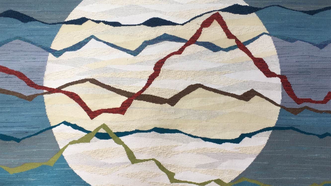 A tapestry showing what could be a full moon on a variegated blue background with colourful strips in foreground