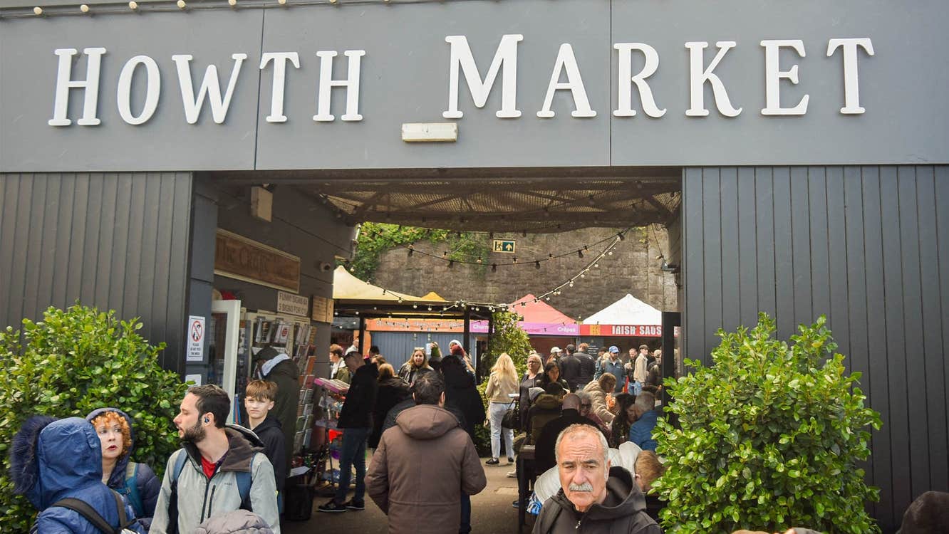 Grey open entrance to a market with a tree either side and people walking through
