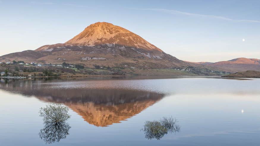 Mount Errigal reflecting onto a lake with the moon in the sky