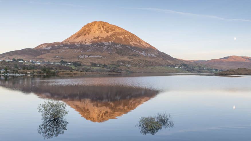 Mount Errigal reflecting onto a lake with the moon in the sky